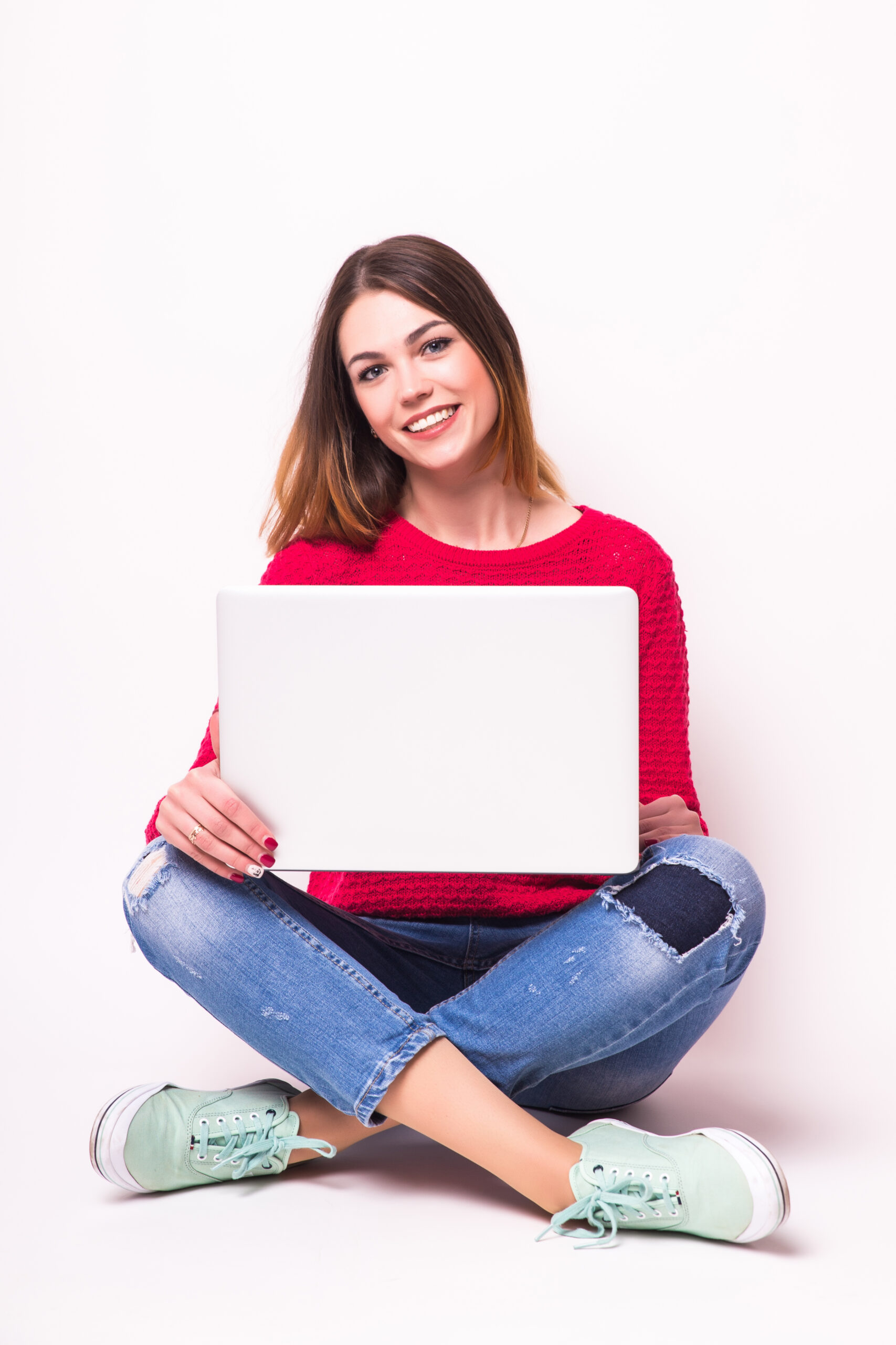 happy young woman sitting on the floor with crossed legs and using laptop on gray background